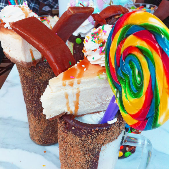 Sugar Daddy Milkshakes served in chocolate frosted mugs sprinkled with graham cracker crumbs & topped with lollipops